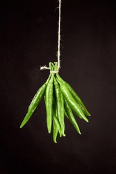 Bunch of green chili peppers hanging on a natural rope on a brown background