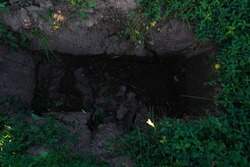 Digged grave in the backyard.  A pit dug in the ground. A grave. Hole in the ground. green grass around. 