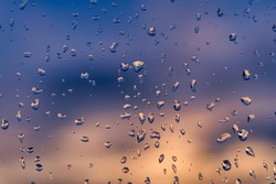 Raindrops on a window with a sunset sky in the background. Clear weather after the rain.