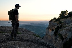 Young man with tactical equipment looks from the summit at sunset while waiting for night to fall