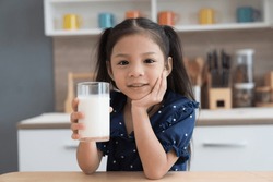 Asian little child girl holding glass of milk in kitchen at home