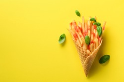 Fried potatoes in waffle cones on yellow background. Hot salty french fries with sauce, basil leaves. Fast food, junk food, diet concept. Top view. Minimal style. Pop art design, creative concept