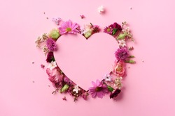 Creative layout with pink flowers, paper heart over punchy pastel background. Top view, flat lay. Spring, summer or garden concept. Present for Woman day.