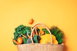 Straw basket with organic vegetables over trendy yellow background. Healthy food, vegetarian diet. Eco friendly, zero waste, plastic free concept