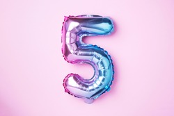 Creative layout. Rainbow foil balloon number and digit five 5. Birthday greeting card. Anniversary concept. Top view. Copy space. Stylish colored numeral over pink background. Numerical digit