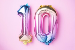 Rainbow foil balloon number, digit ten. Birthday greeting card with inscription 10. Anniversary concept. Top view. Colored numeral on pink background. Numerical digit, Celebration event, template.