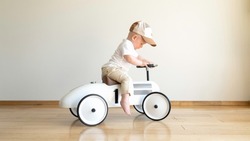 Toddler driving beige retro car. Happy small boy sitting on vintage toy car. Kid playing in nursery room. Happy child riding toy vintage car. Funny kid playing at home.