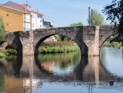 Roman stone bridge located in the Galician city of Monforte de Lemos over the Cabe River on a sunny day projecting its reflection on the flowing water