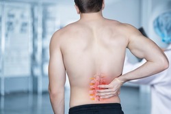 The patient stands and holds on to the spine on a blurred background.