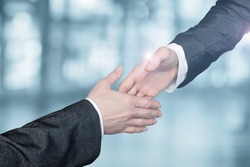 Businessmen reach out to each other to shake hands on a blurred background.