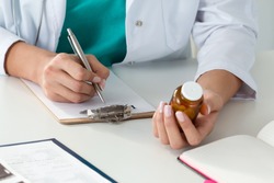 Close-up of doctor's hands writing prescription and holding bottle with pills. Healthcare, medical and pharmacy concept.