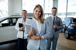 Confident salesteam in dealership, three beautiful consultants or managers in elegant suit looking on camera.