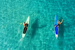 Strong men floating on a SUP boards in a beautiful bay on a sunny day. Aerial view of the men crosses the bay using the paddleboard. Water sports, competitions. Nai Harn beach, Phuket, Thailand.