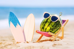 Summer lifestyle image of attractive watermelon surfer lying on sunbed on the sand against turquoise sea. Wearing stylish sunglasses. Surfstyle. Tropical summer vacation concept. Sunbathing on beach