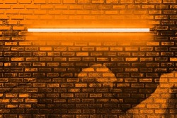 orange neon light bulb on brick wall. Background texture of empty old brick wall with glowing orange neon lamps.