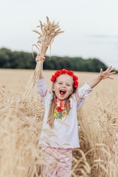 Emotional portrait of a cute and beautiful little girl from Ukraine in a wreath of poppies with blond hair hugging spikelets in a wheat field in the rays of the evening sun. Summer. Harvest concept