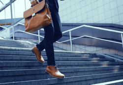 Businessman with bag in his hand walking down steps. Cropped shot of elegant man in suit taking step down on stairs.
