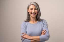 Mongolian Woman with Gray Hair on a Gray Background. She Smiles Broadly. Her Arms are Crossed Before Her. Close Up Shoot.