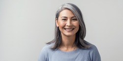 Beautiful Mature Asian Woman Smiles Broadly In Studio. Right Side Tonned Closed-Up Portrait. White Background.