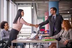Two business teams successfully negotiating, shaking hands. At meeting table business groups shaking hands on completed deal. Man and woman handshake.