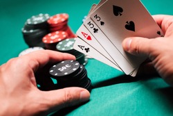 Playing poker in the casino. Cards with two pairs in the hand of the player making a bet with chips on a green table background