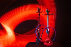 hookahs with hot shisha charcoals in bowls on the table on a dark background with red neon glow