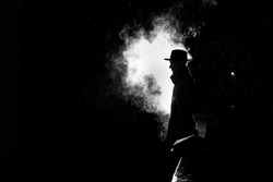dramatic silhouette of a dangerous man in a hat at night in the rain in the city in the old crime 