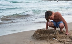 Cute boy on the beach plays with sand. Relax travel concept. Mediterranean sea, Spain