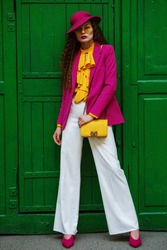 Outdoor full body portrait of young beautiful fashionable woman wearing trendy, colorful clothes, stylish accessories, posing near the green door. Female fashion concept