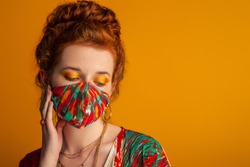 Woman wearing stylish outfit with designer protective bold colors face mask, matching eyes makeup, dress. Trendy Fashion accessory during quarantine of coronavirus pandemic. Copy, empty space for text