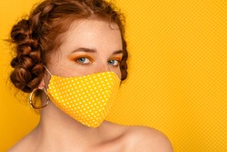 Redhead freckled woman wearing stylish handmade protective yellow polka dot cloth mask. Fashion during quarantine of coronavirus outbreak. Copy, empty space for text
