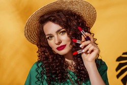 Lipstick advertising conception: beautiful woman with bold fuchsia color lips makeup holding three lipsticks. Summer make up