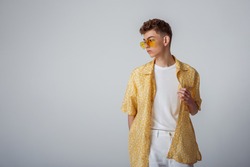 Young fashionable guy wearing trendy sunglasses, yellow shirt, white t-shirt, trousers. Summer fashion conception, studio portrait. Copy, empty space for text