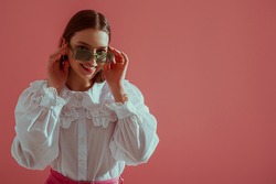 Fashionable  happy smiling girl wearing trendy green rectangular sunglasses, vintage cotton blouse with lace collar, posing on pink background. Copy, empty space for text