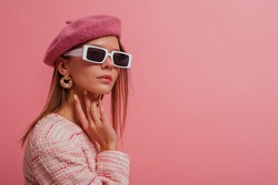Fashionable, elegant woman wearing classic beret, stylish rectangle white frame sunglasses, trendy pearl earrings, posing on pink background. Copy, empty space for text 