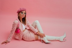 Fashionable, elegant woman wearing  beret, sunglasses, pink tweed suit with mini skirt, white leather over knee boots with high heels, posing with patent leather sholder bag. 
Copy, empty space