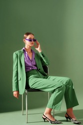  Fashionable beautiful confident woman wearing trendy color sunglasses, suit blazer, classic trousers, purple office shirt, zebra print pointed toe shoes, posing on green background. Fashion portrait