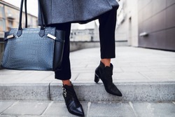Elegant outfit. Close up of textured big dark blue bag. Model posing in street, wearing short trousers, black pointed toe ankle boots. Female fashion concept. Copy, empty space for text
