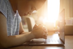 Asian woman praying by faith with computer laptop ,Church services online concept, Home church during quarantine coronavirus Covid-19, Online church from home concept, spirituality and religion