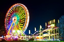 Amusement park at night - ferris wheel and rollercoaster in motion
