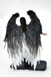 full length portrait of beautiful asian model with dark hair, wearing black gothic skirt costume, angel feather wings with horned headdress. Standing pose  isolated on studio background.