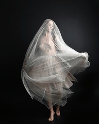 Full length portrait of beautiful woman wearing white gown dress with flowing ghostly veiled fabric, isolated on dark studio background.