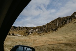 Woman taking photos from the car window of the waterfall in Iceland