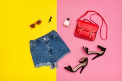 Denim shorts, black shoes, red handbag, sunglasses. Bright yellow and pink background. Fashionable concept