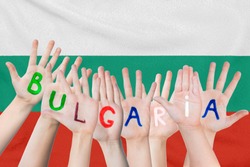 Inscription Bulgaria on the children's hands against the background of a waving flag of the Bulgaria