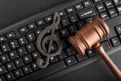Protection of music as intellectual property. Treble clef on the keyboard next to the wooden gavel on black background. Music Licensing
