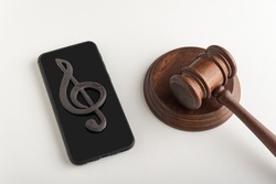 Mobile phone with treble clef sign on display and judges hammer. Illegal use of music concept. Digital piracy
