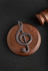 Music symbol treble clef and judge gavel on black background. Music piracy and copyright infringement. Vertical frame.