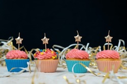 Birthday cupcake with candles in the form of stars in festive tinsel on black background. Space for text