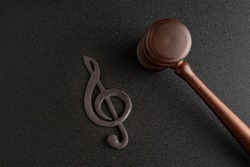 Music copyrights. Treble clef next to gavel on black background. Music piracy concept
